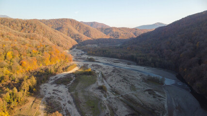 Aerial view of the river valley between mountain ranges. Beautiful winter landscape with colorful forest in the mountains. Shakhe river, Sochi, Russia. 