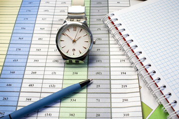On the document with colored columns of numbers are a wrist watch a pen and a Notepad. Business concept
