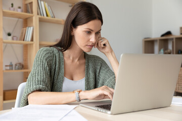 Pensive young Caucasian female worker look at laptop screen think browse internet in office. Thoughtful businesswoman work on computer, consult client or customer online, prepare research on gadget.