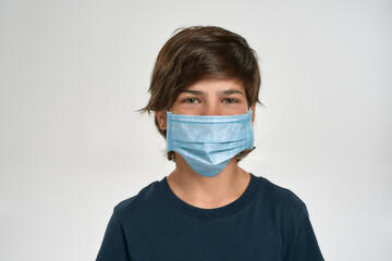 Portrait of little sportive boy child in sportswear wearing medical mask, looking at camera, standing isolated over white background