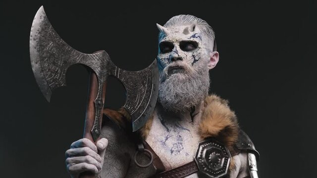 Risen from the dead frosty northern warrior with iced skin and beard posing in dark background with his two handed double axe looking around.