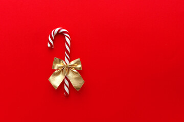 A candy cane with a gold bow on a red tbackground, Christmas Candy.