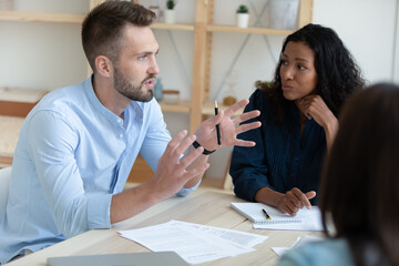 Close up of motivated diverse employees talk in group discuss company financial paperwork in office together. Multiethnic colleagues coworkers brainstorm consider documents at team briefing.
