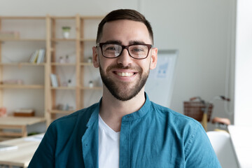 Close up headshot portrait of smiling young Caucasian businessman in glasses posing in office....