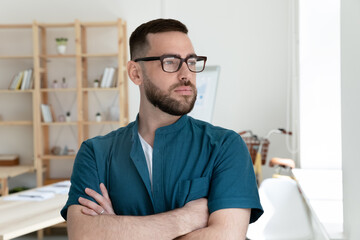 Fototapeta premium Pensive young Caucasian male employee in glasses look in window distance thinking or planning. Thoughtful man worker pondering in office, imagine career opportunity. Business vision concept.