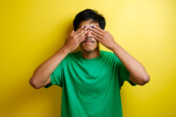 Portrait of asian young man in green t-shirt covering eyes with both hands