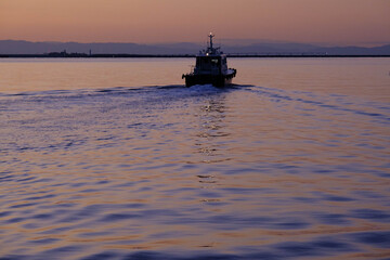 神戸メリケンパークの夜明け。大阪湾に向かって進むボート。朝日に輝く波。
