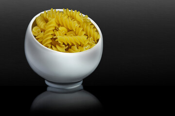 Italian pasta in a porcelain cup. Swirling shape. Black background. Advertising concept with copy space for customized text