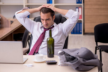 Young male employee drinking alcohol in the office