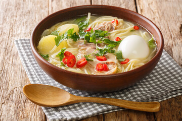 Homemade chicken soup with noodles, potatoes, boiled egg and herbs close-up in a plate on the table. horizontal