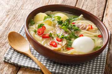 Peruvian food Caldo de Gallina chicken noodle soup with boiled egg and herbs close-up in a plate on the table. horizontal