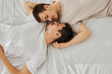 Obraz na płótnie Canvas Young gay couple lying on bed tops to tails top view on white sheet