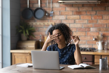 Unhappy young african american woman taking off eyeglasses, feeling tired due to computer overwork. Stressed millennial multiracial lady suffering from eyes strain, having dry eyes syndrome. - Powered by Adobe