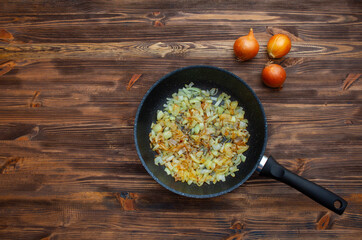 Frying pan with fried onions, three onions side by side. Brown wood background.