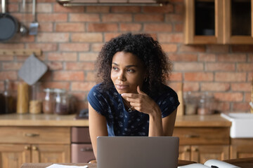 Dreamy young african american woman looking in distance, distracted form laptop work, thinking of...