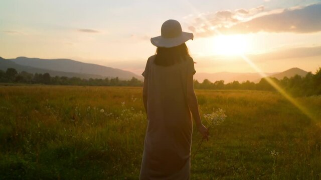 happy summer vacation sky at sunset rear woman in maxi dress enjoy mountains landscape walks holding chamomiles slow motion