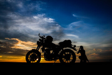 Woman and motorcycle silhouetted against the setting sun