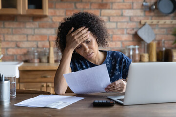 Stressed young african american woman looking at paper bills, feeling confused of high payment...