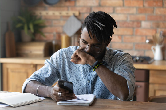 Stressed young biracial guy in glasses feeling confused of getting message with unexpected bad news. Unhappy african man getting bank debt notification on cellphone, thinking of problem solution.