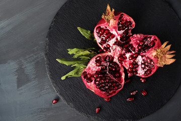 broken into pieces pomegranate fruit with leaves on a black round stand of slate black background