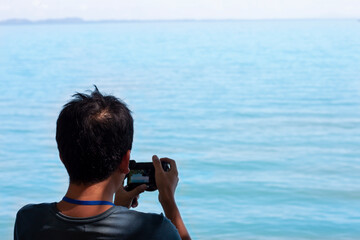 Male tourists stand to take pictures of the sea stay at the coast while traveling on vacation.