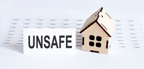 Closeup of house wooden model with blank for text UNSAFE on chart background.