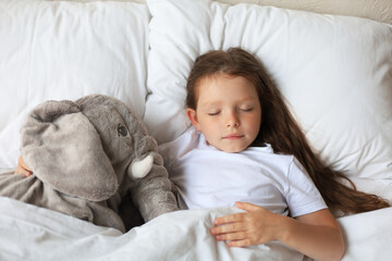 Cute child little girl sleeps in the bed with a toy elephant.