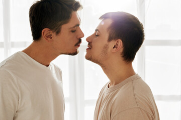 Gay couple of men kissing on white background at home close-up