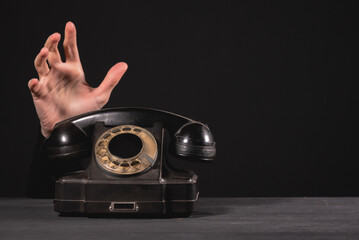 Old retro black rotary phone on the black desk table and woman hands background.