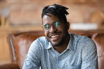 Head shot happy young 30s african american male blogger sitting on comfortable sofa, looking at camera, recording lifestyle video Smiling millennial mixed race man enjoying video call talk at home.