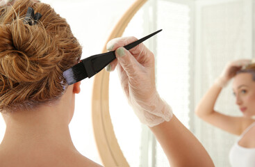 Young woman applying dye on hairs near mirror indoors, closeup