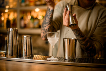 male bartender pouring drink from metal jigger into mixing cup on bar counter