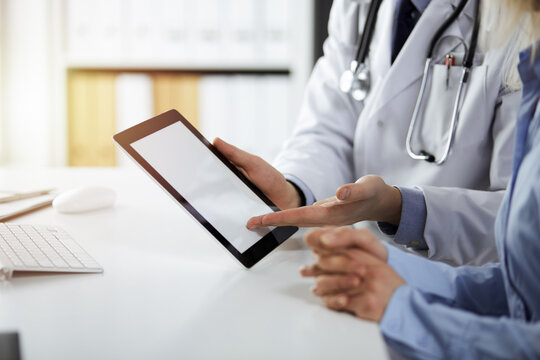 Unknown male doctor and patient woman discussing current health examination while sitting in sunny clinic and using tablet computer. Perfect medical service in hospital