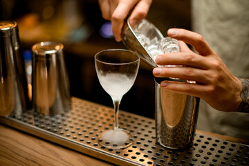 man bartender holds metal scoop with ice in his hand and pours it into mixing cup.