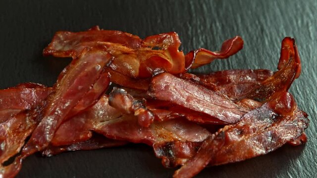 Super Slow Motion Shot of Roasted Bacon Slices Falling on Black Table at 1000 fps.