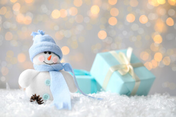 Snowman toy on snow against blurred festive lights, space for text. Christmas decoration