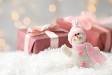 Snowman toy and Christmas gift boxes on snow against blurred festive lights. Space for text