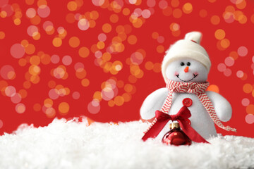 Snowman toy and Christmas ball on snow against blurred festive lights. Space for text