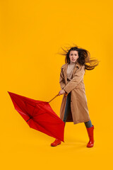 Emotional woman with umbrella caught in gust of wind on yellow background