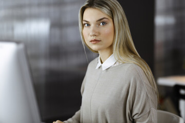 Blonde business woman sitting and looking at camera in office. Business headshot portrait