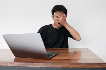 Young asian man hiding his face with hand because shocked and embarrassed by some porn videos or...