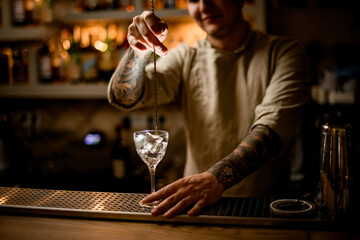 view on man bartender with long bar spoon stir the ice cubes in wine glass