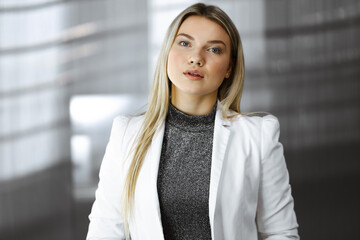 Young blonde business woman or female student in white blazer is standing straight and posing at camera. Lifestyle and diverse people concept - 397561420