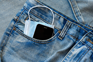 Blue medical mask and black smartphone in the pocket of blue jeans.