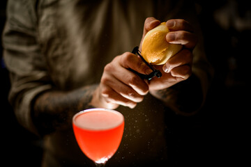 close-up view on barman holds lemon and accurate cuts the peel off with knife