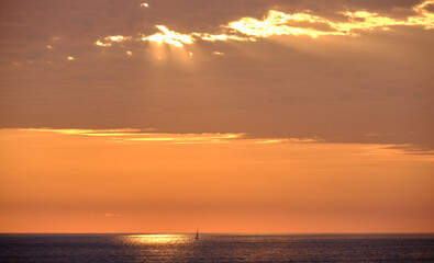 rayos de sol entre una nube iluminando el mar con un barco a la derecha