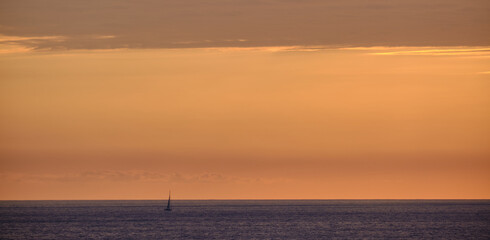 luz anaranjada al atardecer con un velero en el lado izquierdo