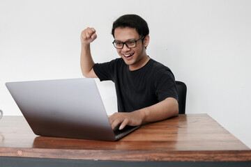 Happy excited Asian man with laptop and raising his arm up to celebrate success or achievement.