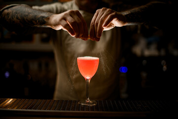 view of bartender holding lemon peel and skillfully sprinkles on glass with bright cocktail.