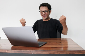 Happy excited Asian man with laptop and raising his arm up to celebrate success or achievement.